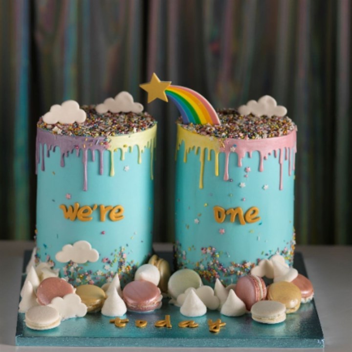 Two colorful birthday cakes with rainbow and cloud decorations on a blue base.