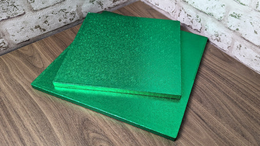 Two green square cake drums placed on a wooden surface.